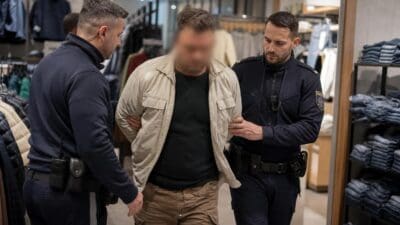 Zwei Polizisten führen einen Mann mit verpixeltem Gesicht durch ein Bekleidungsgeschäft