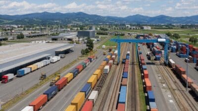 Luftbild eines großen Güterbahnhofs mit bunten Containern auf Zügen und Kränen vor Bergen