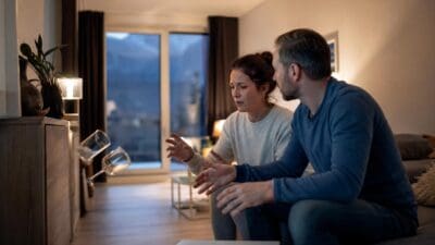 Eine besorgte Frau und ein Mann beobachten zwei fallende Weingläser in einem Wohnzimmer.