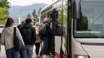 Personen mit Rucksäcken steigen von hinten in einen weißen und roten Bus ein