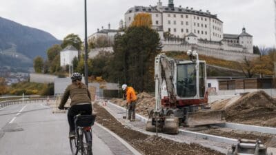 Radfahrerin auf einem Radweg neben Baustelle mit Bagger und Arbeiter vor Schloss Ambras
