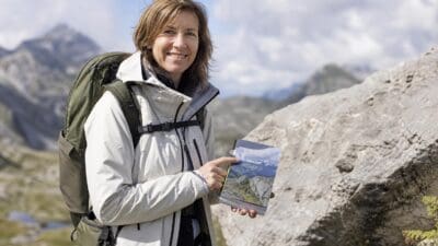 Eine Frau mit Wanderrucksack hält einen Wanderführer in den Bergen