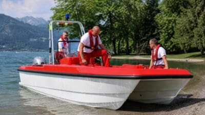 Weiß-rotes Rettungsboot mit drei Männern in roten Westen am Seeufer