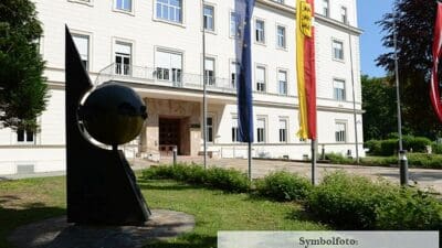 Weißes Amtsgebäude der Landesregierung mit EU-Flagge, Kärntner Flagge und Skulptur im Vordergrund