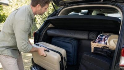 Mann belädt den Kofferraum eines Autos mit einem Koffer und weiterem Gepäck