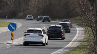 Mehrere Autos fahren hintereinander auf einer kurvigen Autobahn, links ein blaues Verkehrsschild mit Pfeil.