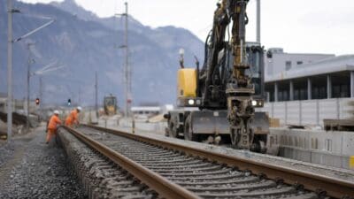 Gelber Bagger auf Bahngleisen bei Bauarbeiten mit zwei Arbeitern in orangen Westen