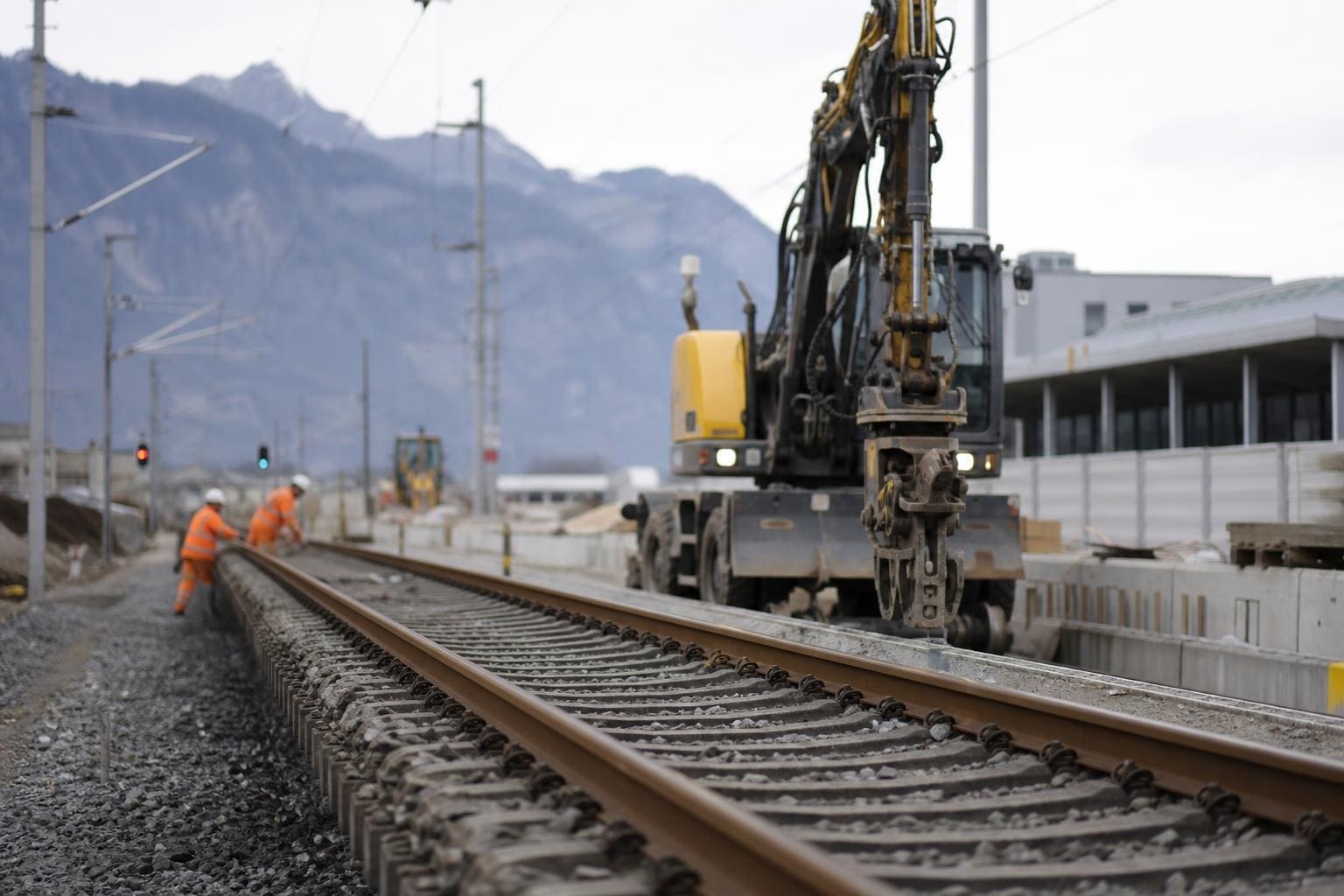 Gelber Bagger auf Bahngleisen bei Bauarbeiten mit zwei Arbeitern in orangen Westen