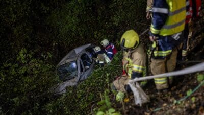 Beschädigtes Auto liegt nachts im Waldhang, Rettungskräfte stehen am Unfallort