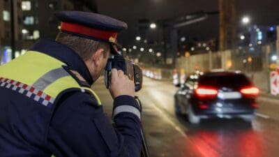 Polizist in Uniform mit Warnweste zielt mit Radarpistole auf ein Auto bei Nacht