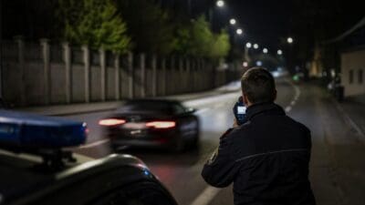 Polizist mit Laserpistole zielt auf ein vorbeifahrendes Auto bei Nacht auf einer Straße
