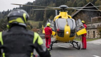 Gelber Rettungshubschrauber mit geöffneten Türen und Einsatzkräften in roter Schutzkleidung auf einer Straße