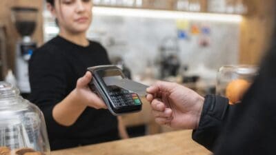 Eine Frau hält ein Kartenlesegerät während eine Hand eine Bankkarte einführt