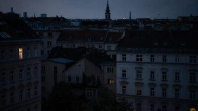 Dunkle Dächer von Wohnhäusern in Wien bei Dämmerung mit beleuchteten Fenstern und Kirchturm