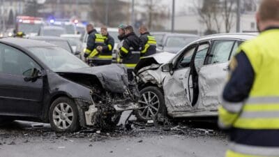 Zwei stark beschädigte Autos nach Frontalkollision auf einer Straße mit Einsatzkräften