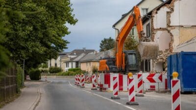 Eine Straße mit Absperrungen und einem Bagger vor einem abgerissenen Haus in Klagenfurt.