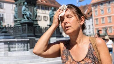 Schwitzende Frau wischt sich mit einem Taschentuch die Stirn vor einem Denkmal
