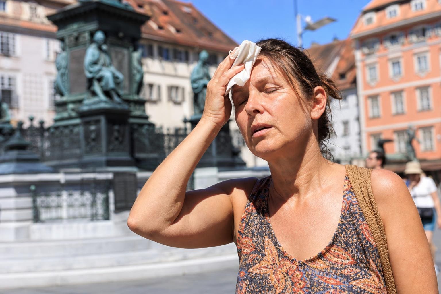 Schwitzende Frau wischt sich mit einem Taschentuch die Stirn vor einem Denkmal