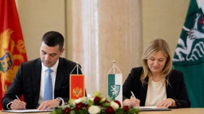 Ein Mann und eine Frau unterzeichnen ein Abkommen an einem Tisch mit Flaggen von Montenegro und der Steiermark