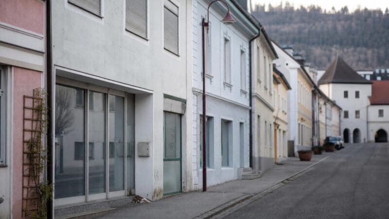 Leere Straße mit mehrgeschossigen Gebäuden und geschlossenen Rollläden in einer Kleinstadt