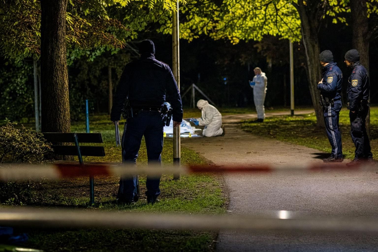 Polizisten und Spurensicherung am abgesperrten Tatort in einem nächtlichen Park