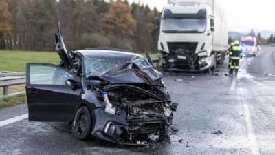 Schwer beschädigtes schwarzes Auto nach Frontalkollision mit Lkw auf der Straße