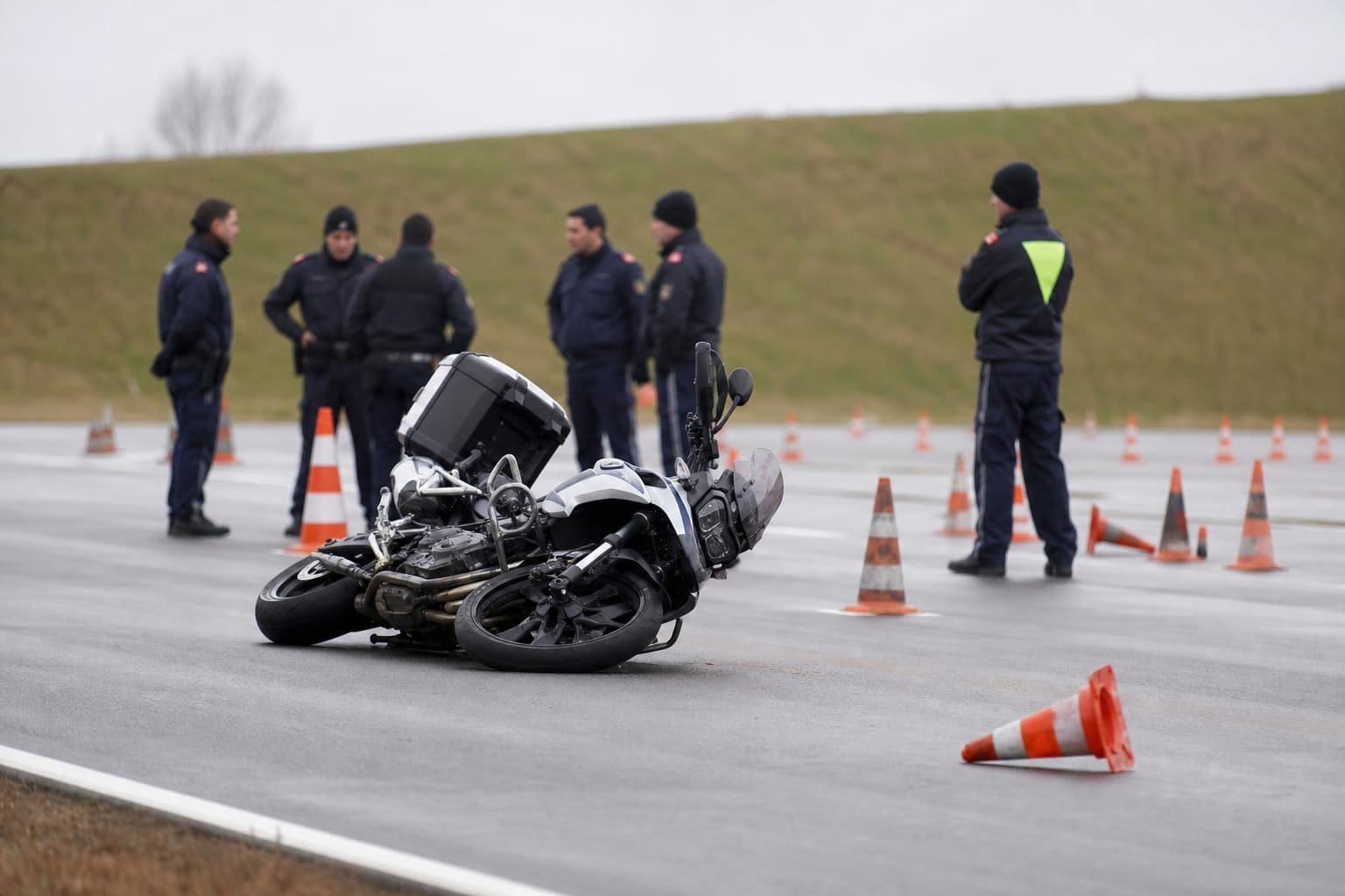 Umgestürztes Polizeimotorrad liegt auf einer asphaltierten Fläche mit Verkehrskegeln und Polizisten im Hintergrund