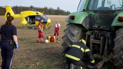 Rettungskräfte und gelber Hubschrauber neben grünem Traktor auf einem Feld