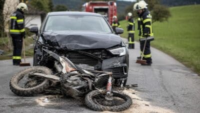 Zusammengestoßenes Motorrad und beschädigtes Auto nach Frontalzusammenstoß auf einer Landstraße mit Feuerwehrleuten
