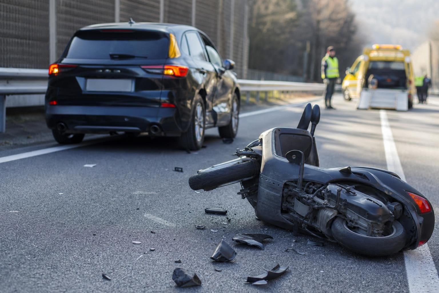Schwarzer Pkw und umgestürzter Motorroller nach Unfall auf Autobahn mit Einsatzkräften im Hintergrund