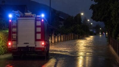 Feuerwehrfahrzeug mit Blaulicht auf überfluteter Straße in der Neulandstraße bei Nacht