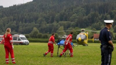 Sanitäter schieben eine Trage mit Ausrüstung zu einem gelben Hubschrauber auf einer Wiese.