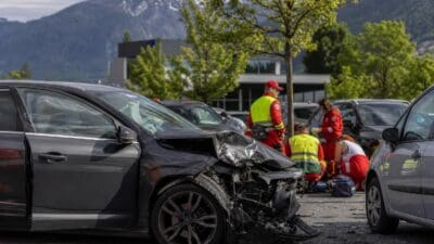 Zerstörtes schwarzes Auto nach Unfall auf Parkplatz mit Rettungskräften