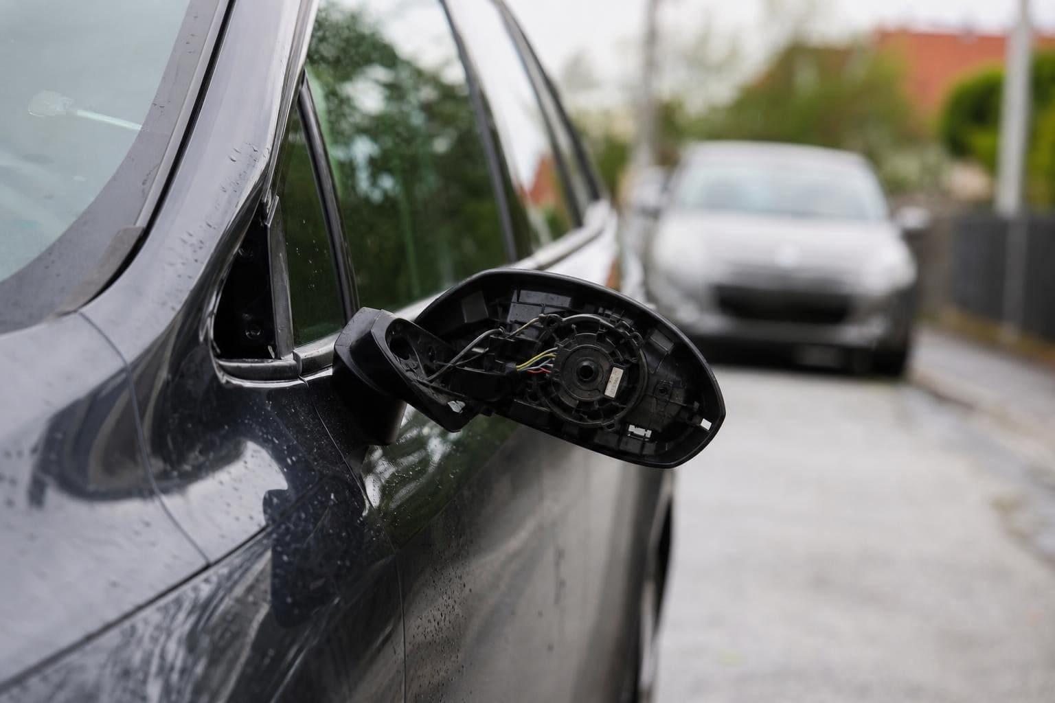 Beschädigter Seitenspiegel eines schwarzen Autos mit freiliegenden Kabeln