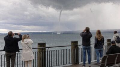 Mehrere Personen stehen an einem Geländer und fotografieren eine Wasserhose über dem Bodensee.