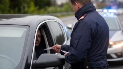Polizist in Uniform übergibt Dokument an Fahrer eines dunklen Autos bei Verkehrskontrolle