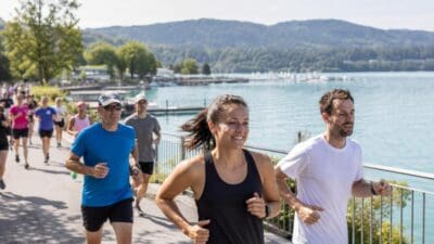 Läuferinnen und Läufer rennen am Ufer des Wörthersees bei sonnigem Wetter