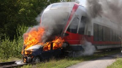 Ein Zug mit roter Front schleift ein brennendes Auto auf den Gleisen mit