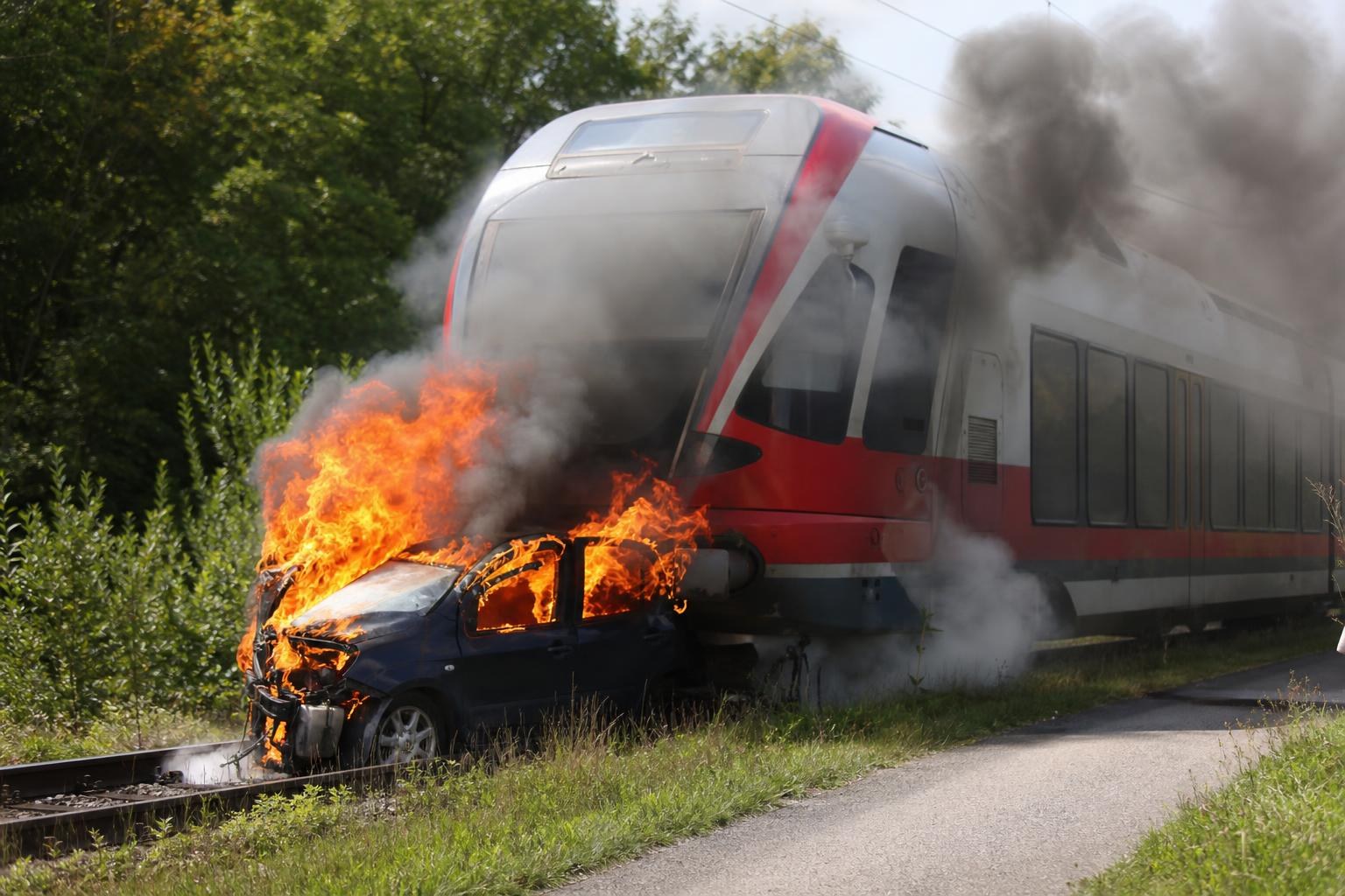 Ein Zug mit roter Front schleift ein brennendes Auto auf den Gleisen mit