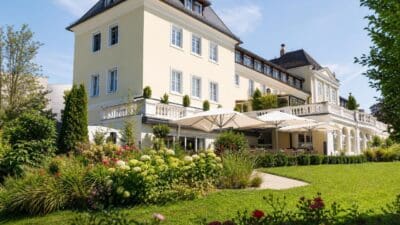 Gelbes mehrstöckiges Hotelgebäude mit weißen Sonnenschirmen in blühendem Garten