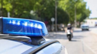 Nahaufnahme eines blauen Blaulichts auf einem Polizeifahrzeug mit einem Motorrad im unscharfen Hintergrund