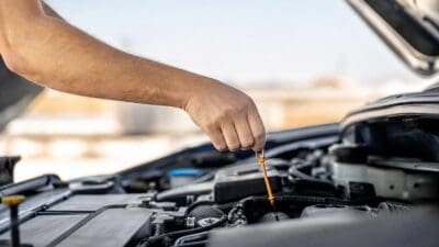 Ein Arm hält einen orangefarbenen Ölmessstab über einem geöffneten Motorraum eines Autos.