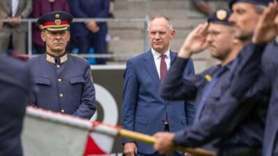 Polizist in Uniform steht neben Mann im Anzug bei Zeremonie mit salutierenden Beamten und Fahne