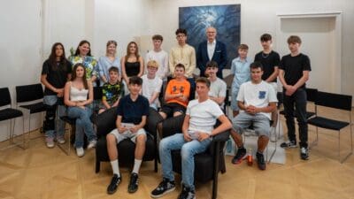 Schülerinnen und Schüler der Polytechnischen Schule Jenbach posieren gemeinsam mit einem Mann im Anzug in einem Besprechungsraum