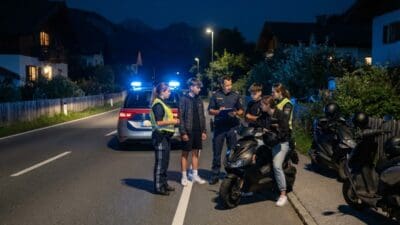 Polizeibeamte in Uniform und Warnwesten sprechen mit Jugendlichen neben mehreren Mopeds auf einer Straße bei Nacht