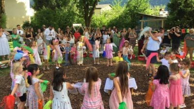 Kinder in bunten Kostümen tanzen mit farbigen Tüchern im Kreis bei einem Fest