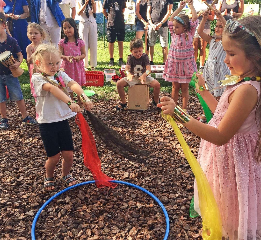 Kinder tanzen mit bunten Tüchern bei einem Sommerabschlussfest im Kindergarten.