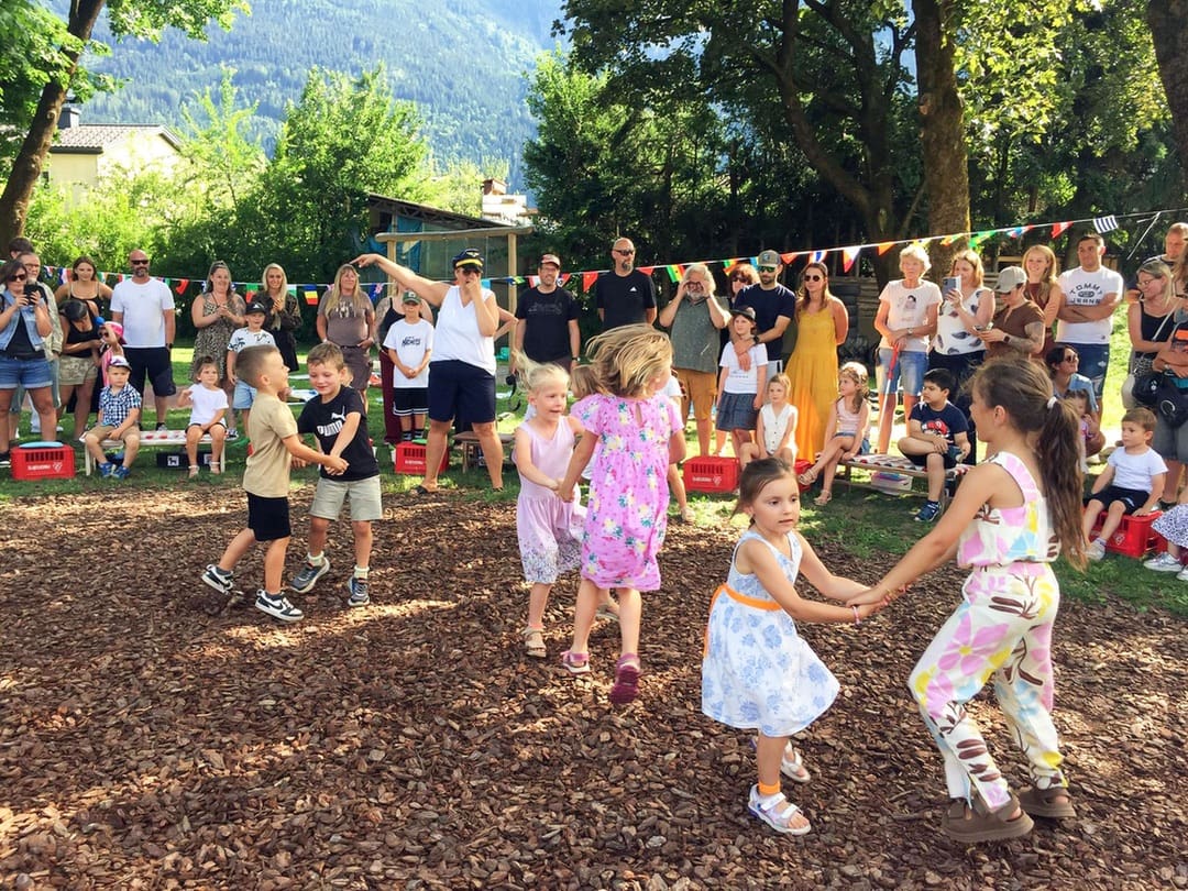 Kinder halten sich an den Händen und tanzen im Kreis auf einem Festplatz mit Holzspänen