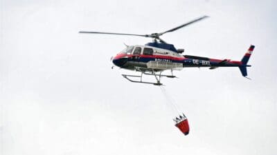 Polizeihubschrauber mit rotem Wasserbehälter an Seilen im Flug