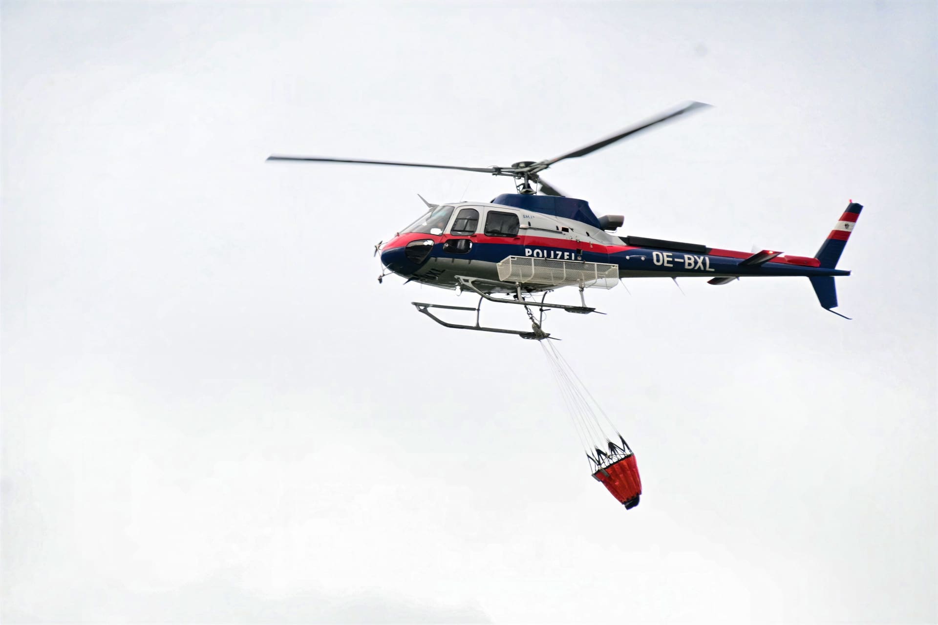 Polizeihubschrauber mit rotem Löschbehälter fliegt am Himmel